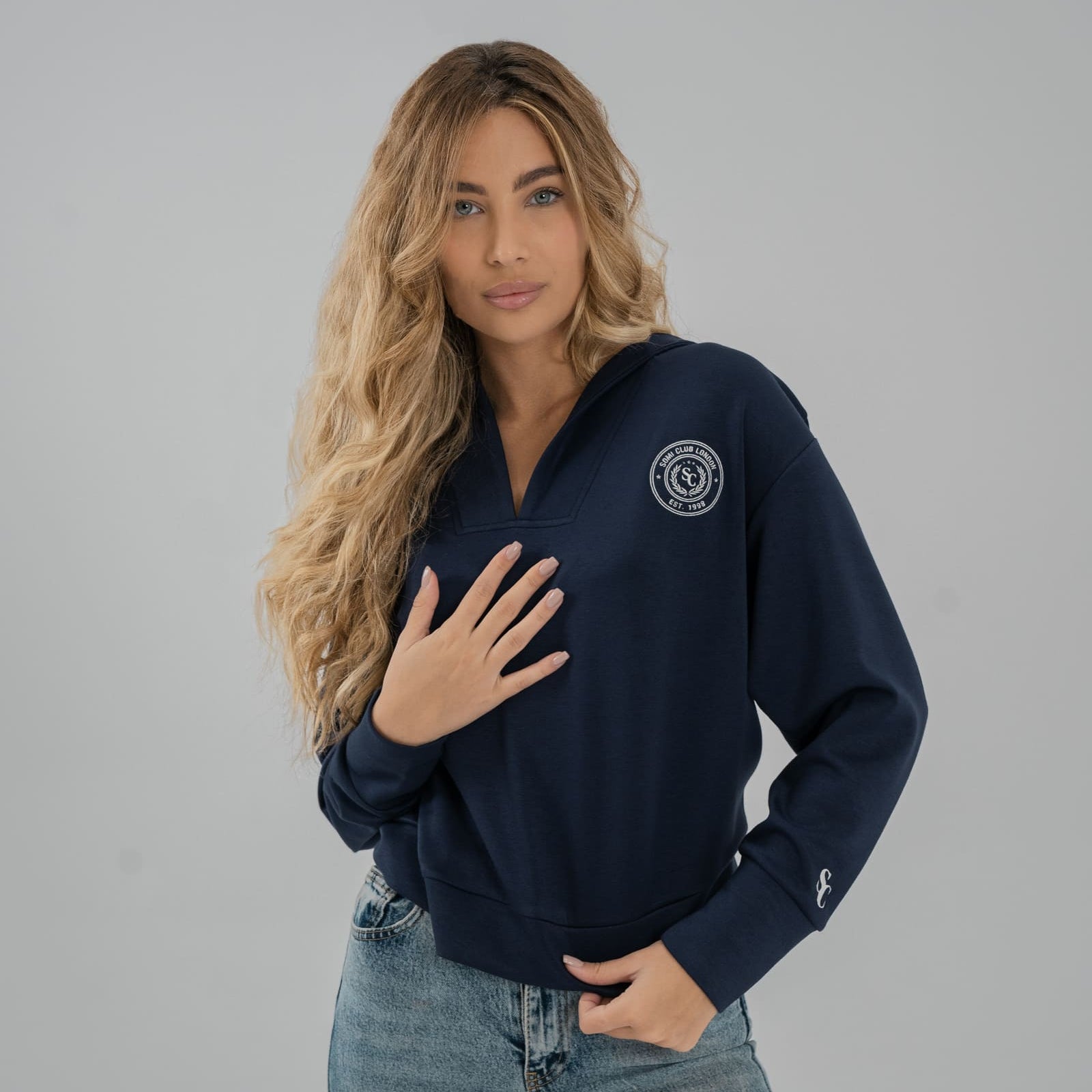 Woman wearing a navy blue SOMI sweatshirt with a logo on a gray background
