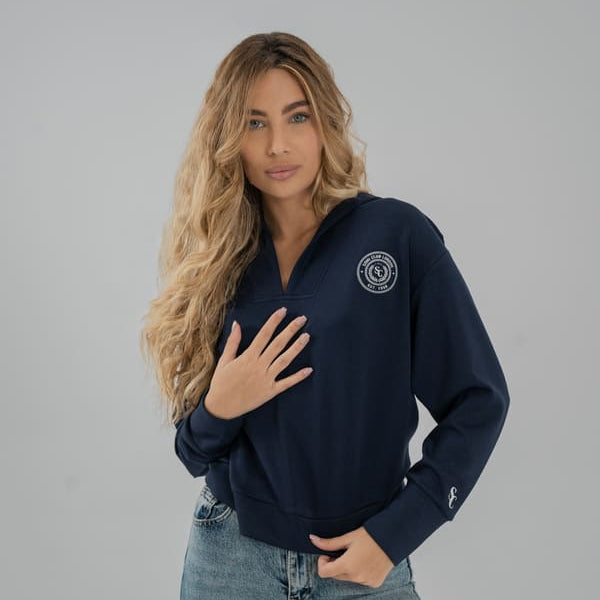 Woman wearing a navy blue SOMI sweatshirt with a logo on a gray background