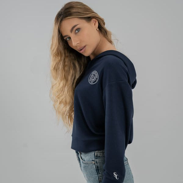 Woman wearing a navy blue SOMI sweatshirt with a logo on a gray background